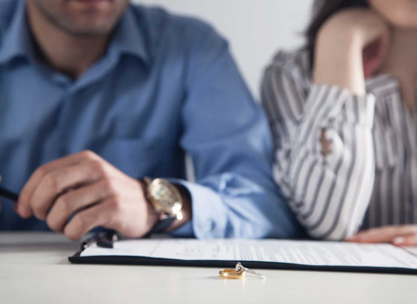 A couple sits at a table with divorce papers and wedding rings placed on the document.