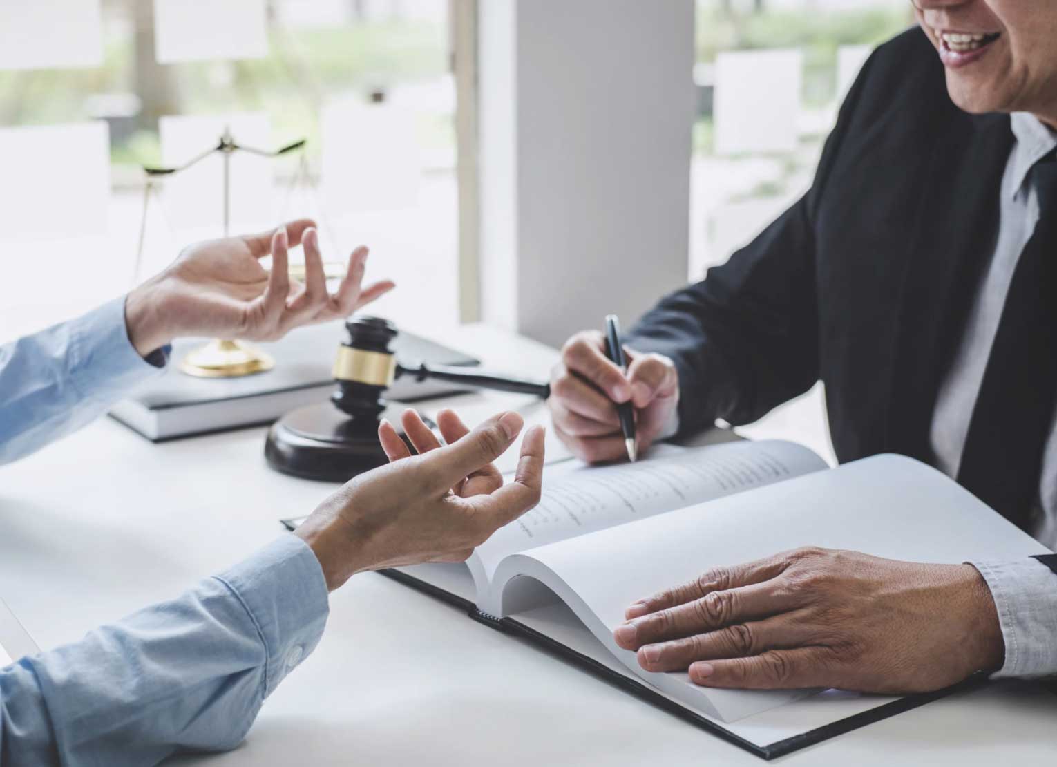 Two people sit at a desk discussing legal documents, with a gavel and scales of justice nearby.